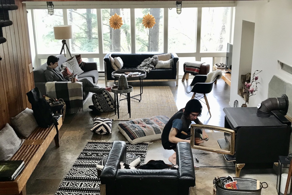 two people relaxing in a cabin, one by the fire the other sitting on a couch.